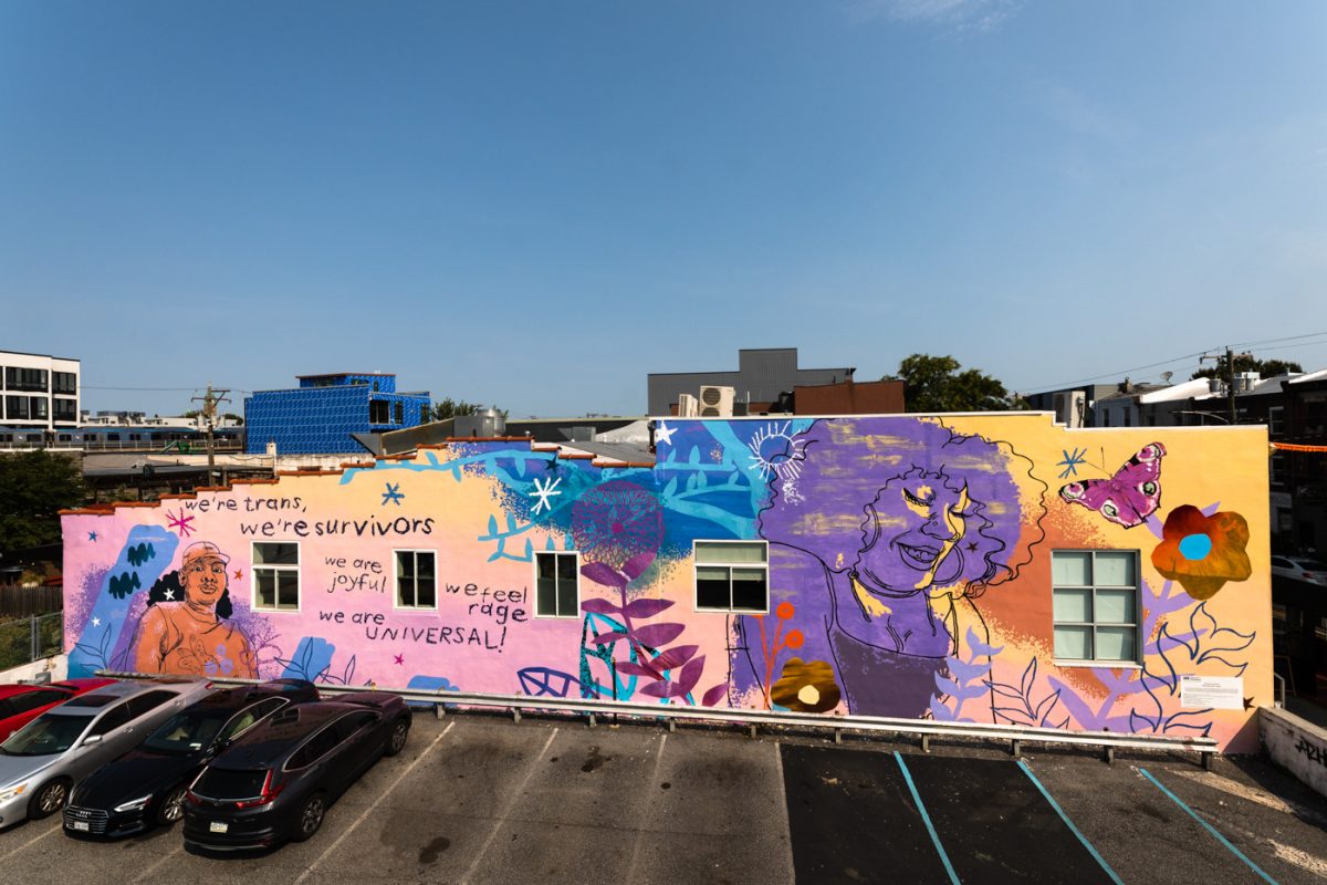 documentation of a Kah Yangni mural at cake life bake shop in Philadelphia, mural is colorfully illustrated with people and butterflies, with text that states "we're trans, we're survivors, we are joyful, we are universal"